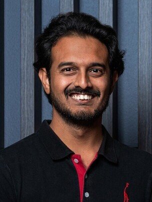 Porträt von Sameran Banerjee in schwarzem Hemd mit rotem Akzent, vor dunklem Hintergrund.